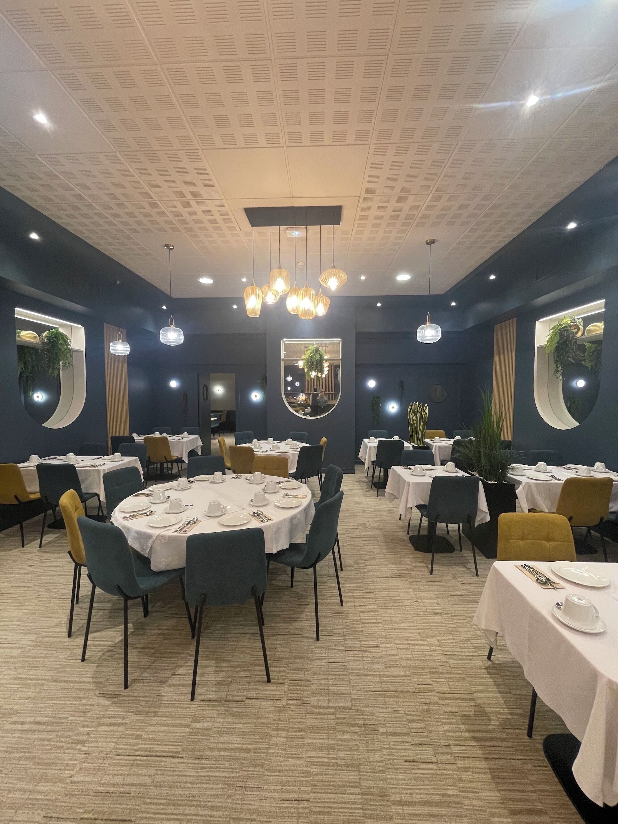 A dining area with round tables, chairs, and overhead lighting.