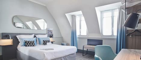 A modern hotel room with a bed, bedside table, lamp, chair, and a desk with a lamp.