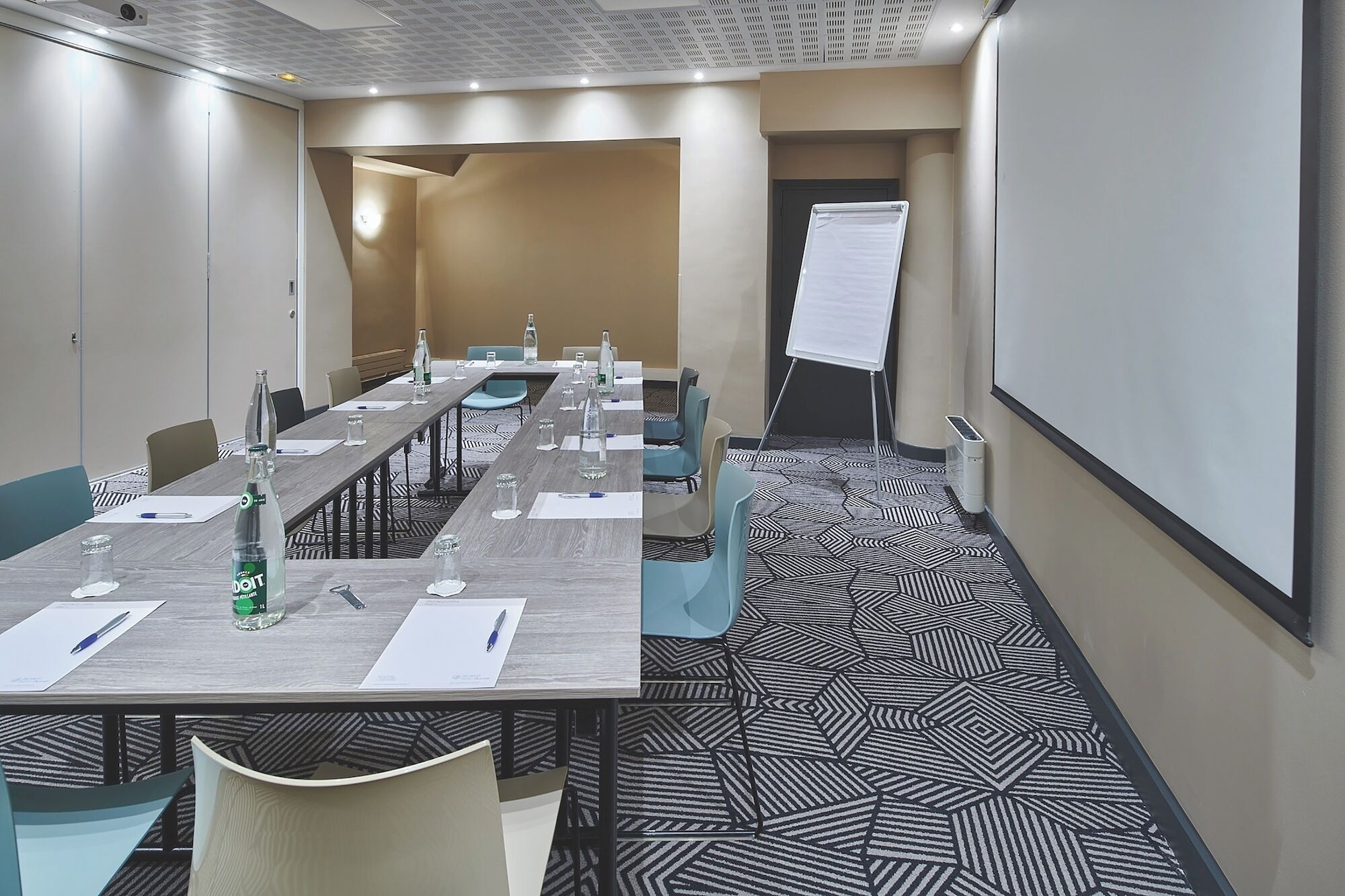 A conference room with a long table, chairs, a whiteboard, and a projector screen.