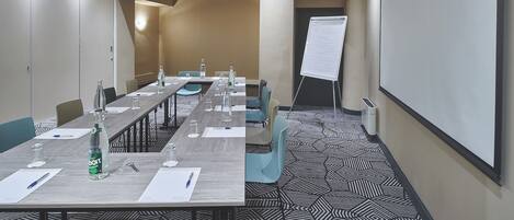 A conference room with a long table, chairs, a whiteboard, and a projector screen.