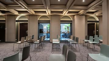 Sala de conferências com várias cadeiras, carpete estampado e vista para uma área externa com mesas e cadeiras.