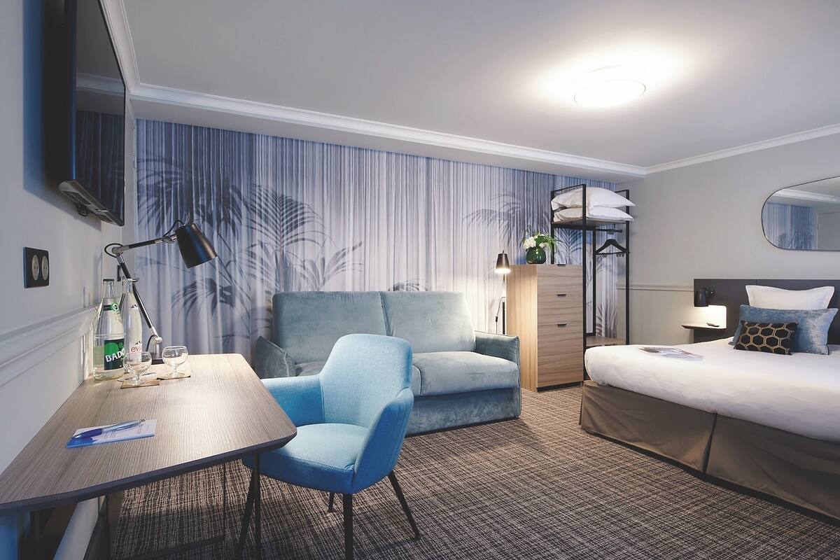 A hotel room with a bed, a desk, a chair, a dresser, and a mirror.