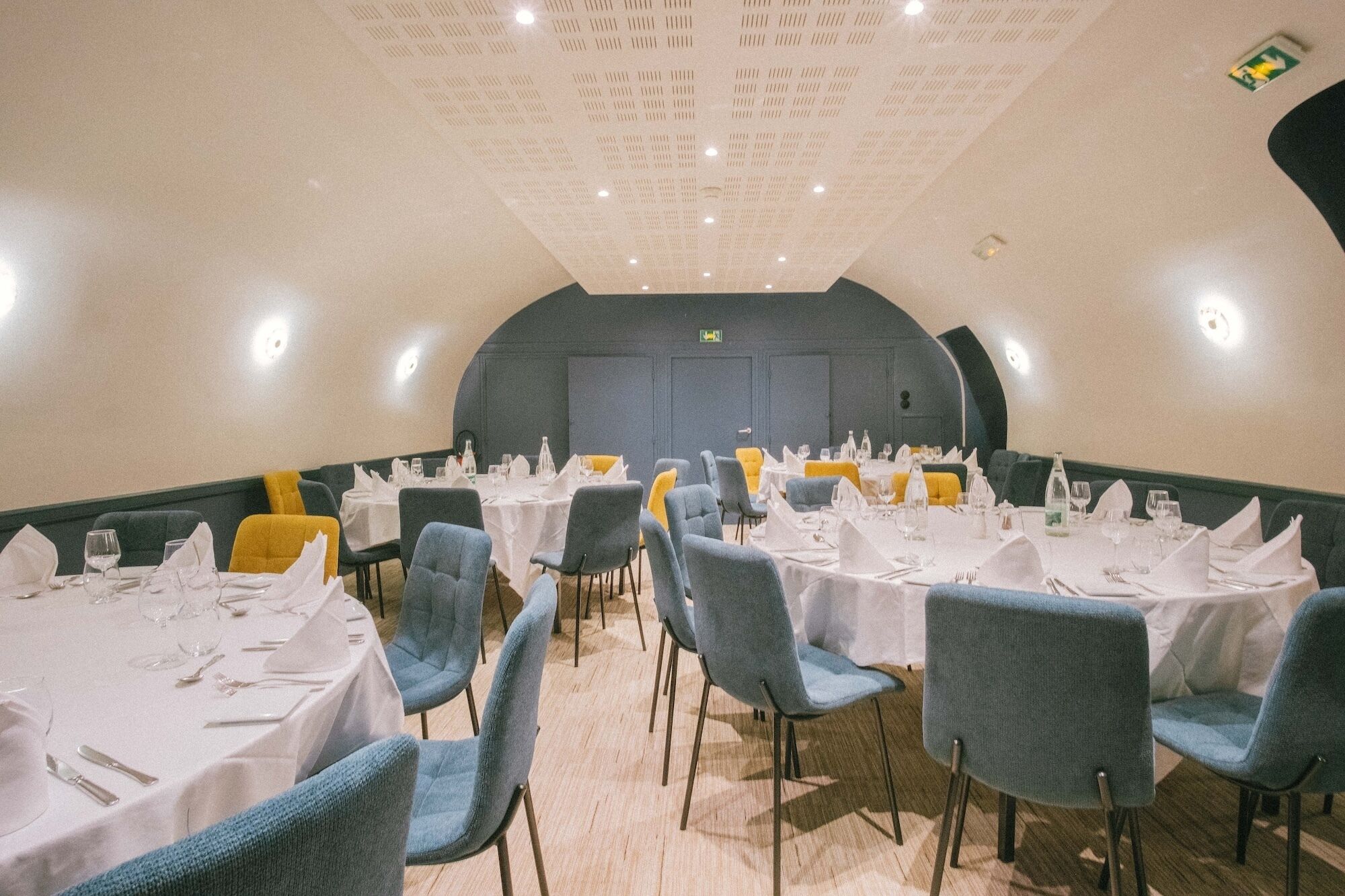 A dining area with round tables, chairs, and a high ceiling with a geometric pattern.