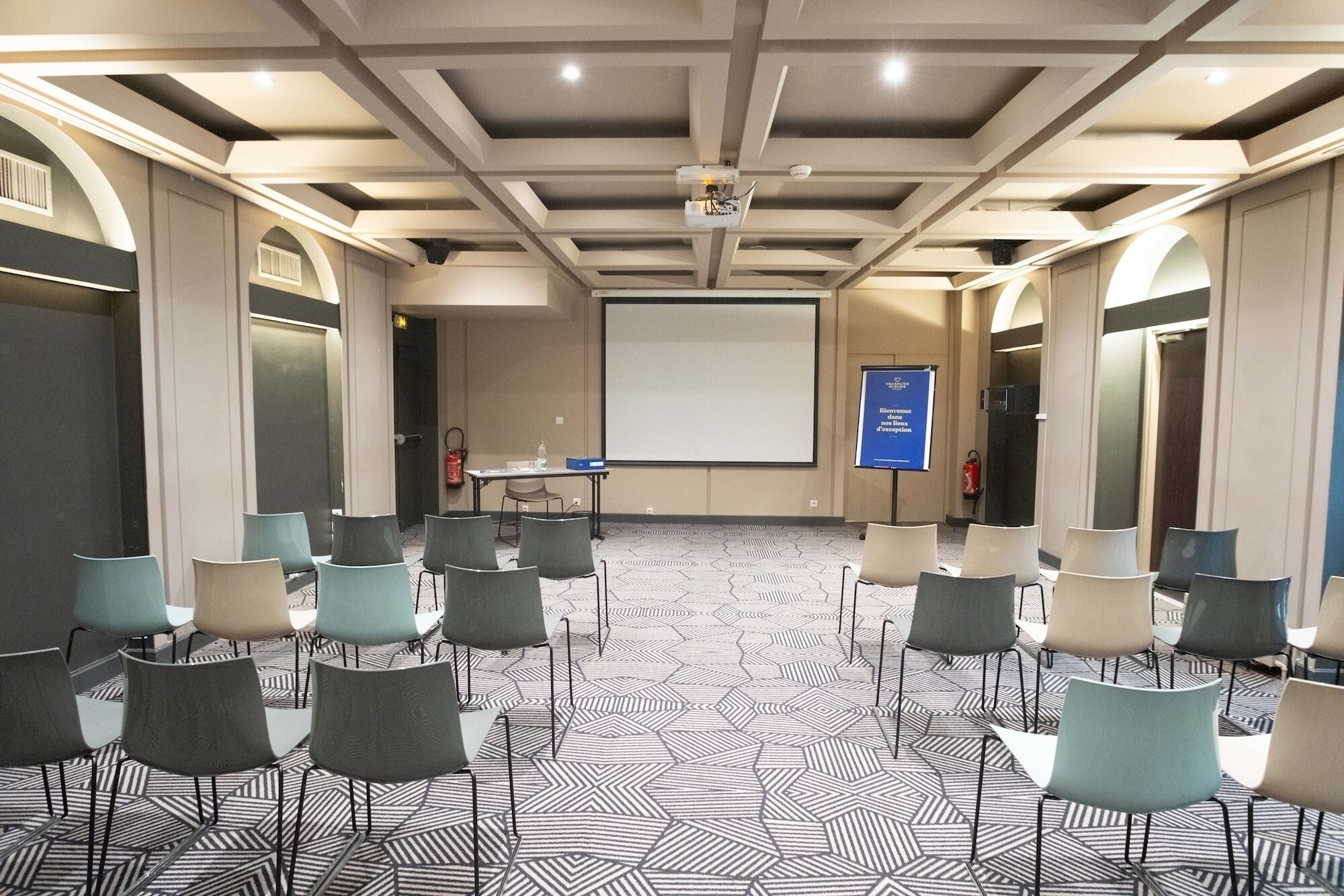 Un salón de conferencias con una pantalla grande, sillas dispuestas en filas y un suelo con diseño.