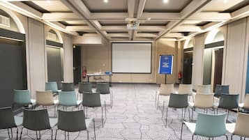 Un salón de conferencias con una pantalla grande, sillas dispuestas en filas y un suelo con diseño.