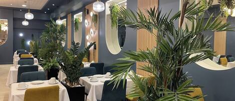 A restaurant with tables set for dining, plants, and modern lighting fixtures.