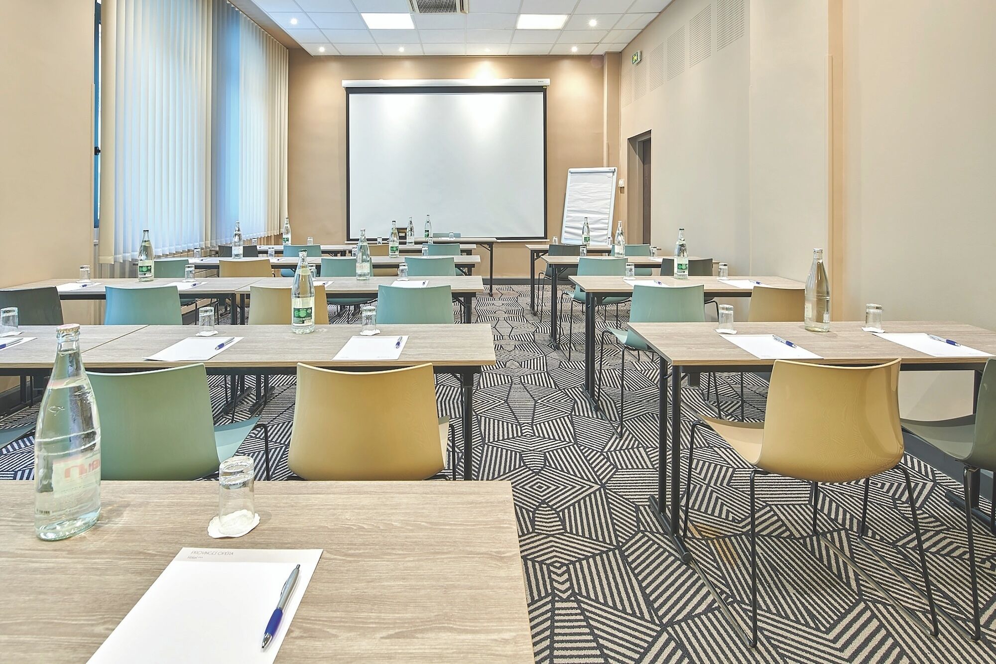 A conference room with multiple tables, chairs, a projector screen, and a whiteboard.