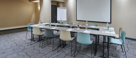 A conference room with a long table, chairs, a projector screen, and a whiteboard.