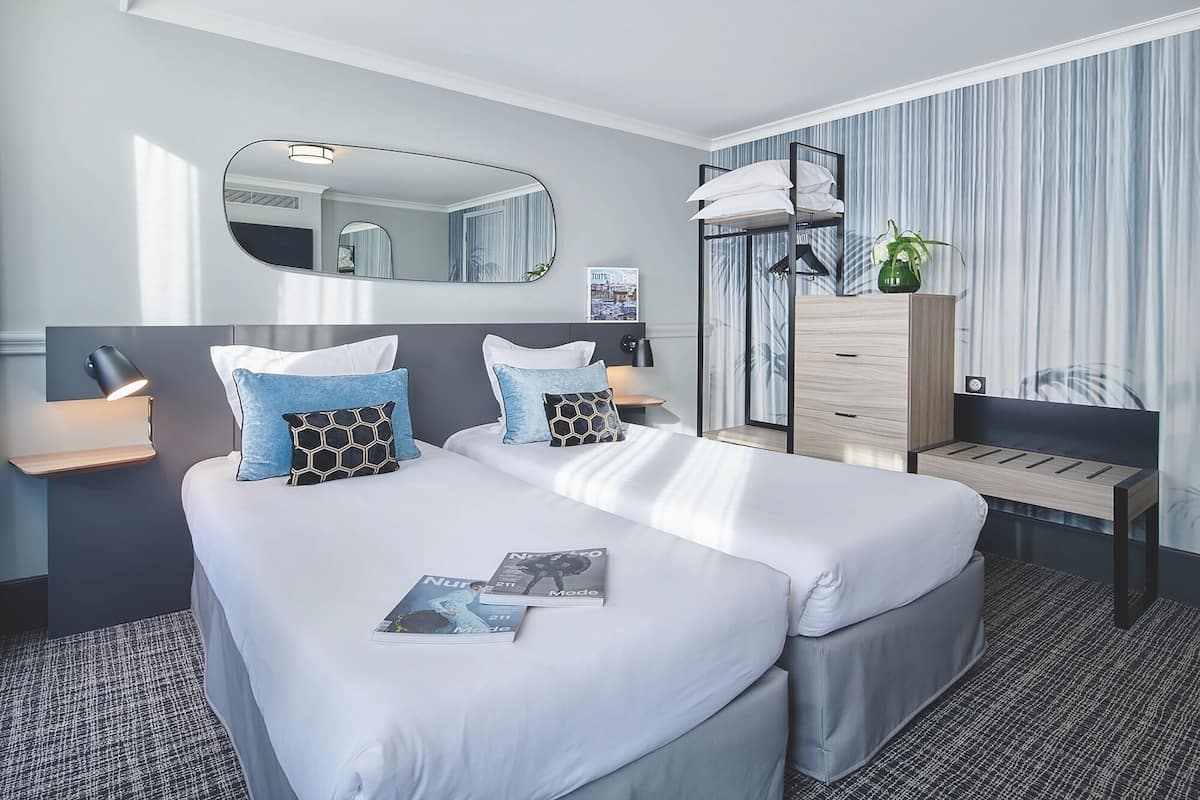 A hotel room with a double bed, bedside tables, a mirror, a dresser, and a window with curtains.