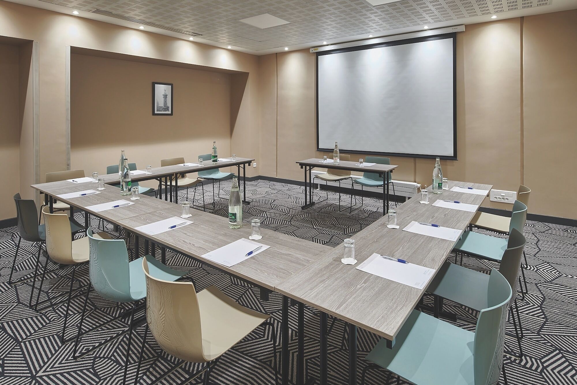 Ein Konferenzraum mit einem großen Tisch, Stühlen, einer Projektionsleinwand und einem gemusterten Teppich.