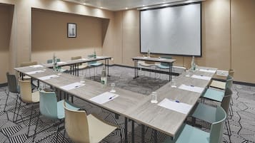 Ein Konferenzraum mit einem großen Tisch, Stühlen, einer Projektionsleinwand und einem gemusterten Teppich.