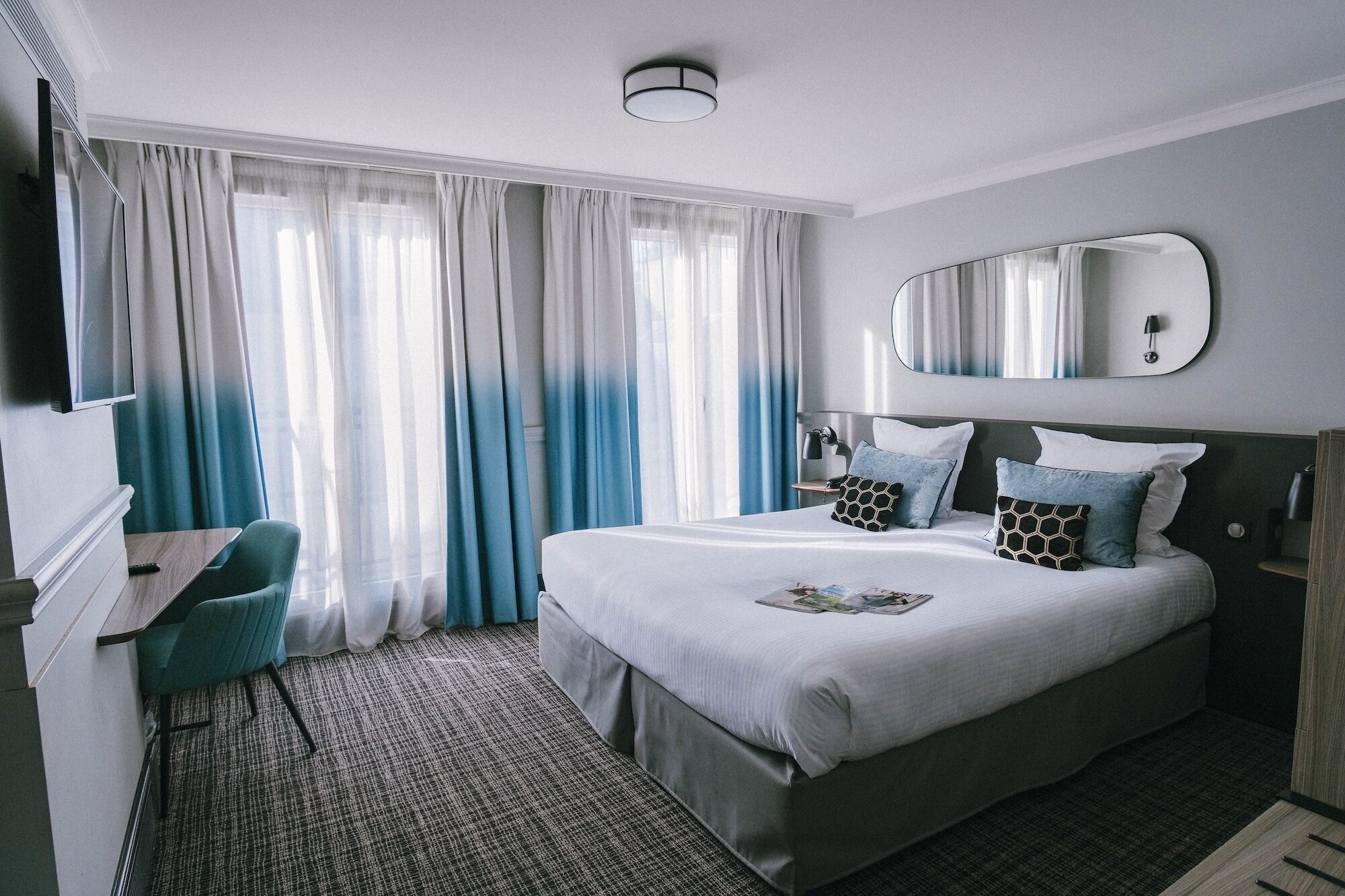 Habitación de hotel con una cama grande, un escritorio, una silla, un espejo y una ventana con cortinas.