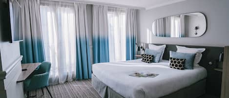 Ein Hotelzimmer mit einem großen Bett, einem Schreibtisch, einem Stuhl, einem Spiegel und einem Fenster mit Vorhängen.