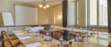 A conference room with a long table, chairs, water bottles, and a projector screen.
