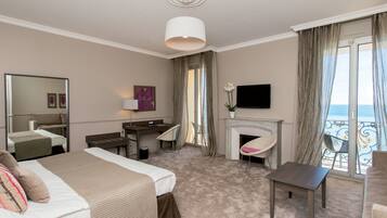 A hotel room with a bed, desk, chair, TV, fireplace, and a balcony with a view.