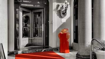 L’entrée d’un hôtel, avec une porte en verre, un tapis rouge et une statue d’une femme portant une robe rouge.