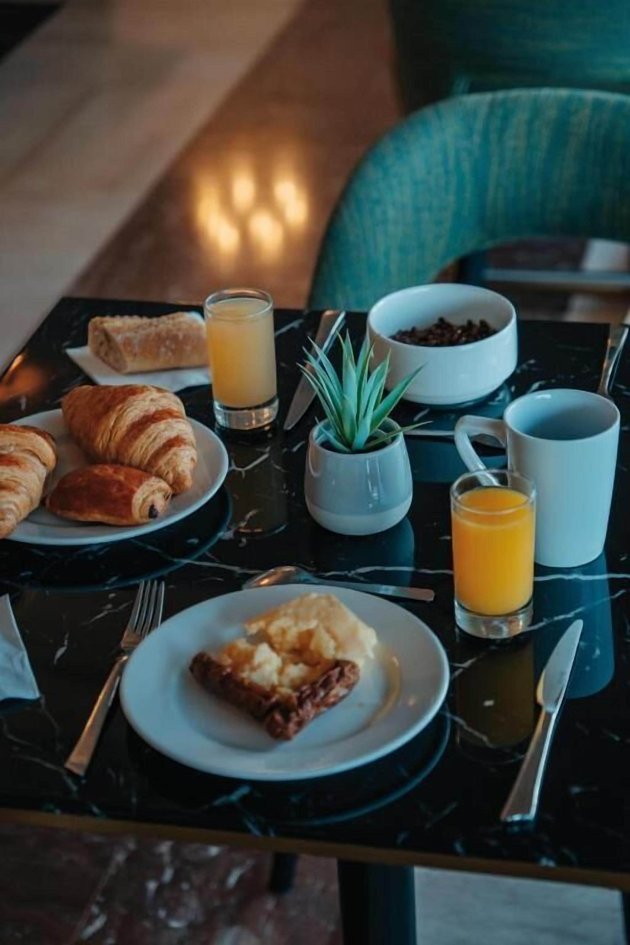A breakfast table with croissants, orange juice, and a bowl of coffee beans.