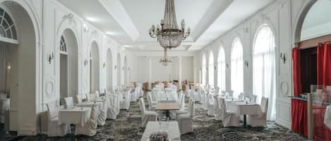 A formal dining room with multiple tables, white chairs, and a chandelier.