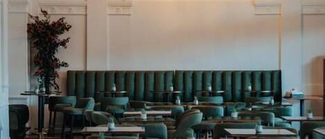A restaurant with green upholstered booths and tables, a chandelier, and a columned ceiling.