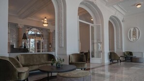 Un vestíbulo amplio con techos altos, arcos y piso a cuadros. Hay sofás y sillones dispuestos para sentarse.