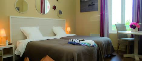 Camera d'albergo con due letti, un comodino, una sedia, un tavolo con un vaso e una finestra con tende.