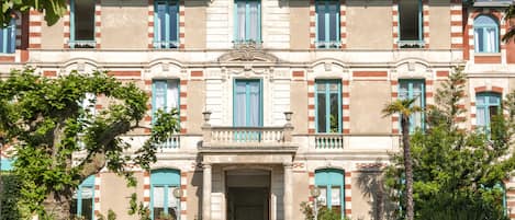 A historic building with a symmetrical facade, multiple balconies, and a central entrance with steps.