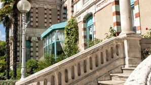 A grand staircase leading to a building with a classical architectural style, featuring a balustrade and a palm tree nearby.