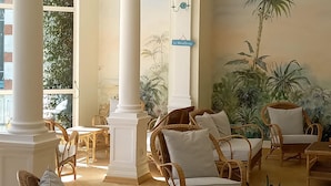 A spacious lounge area with wicker furniture, white columns, and a mural of a palm tree.