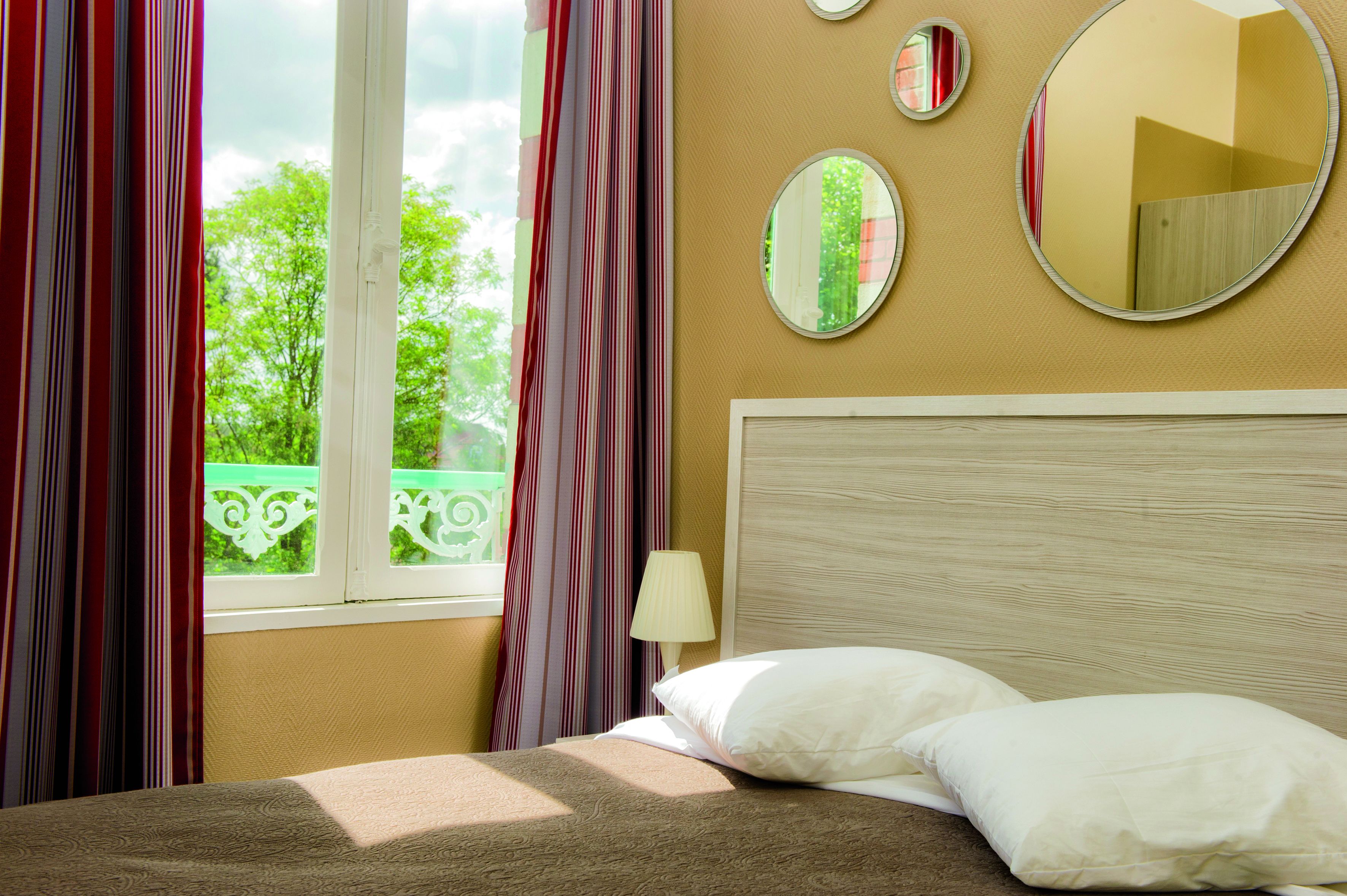 Habitación de hotel con cama, ventana con cortinas, espejo en la pared y vista a zonas verdes.