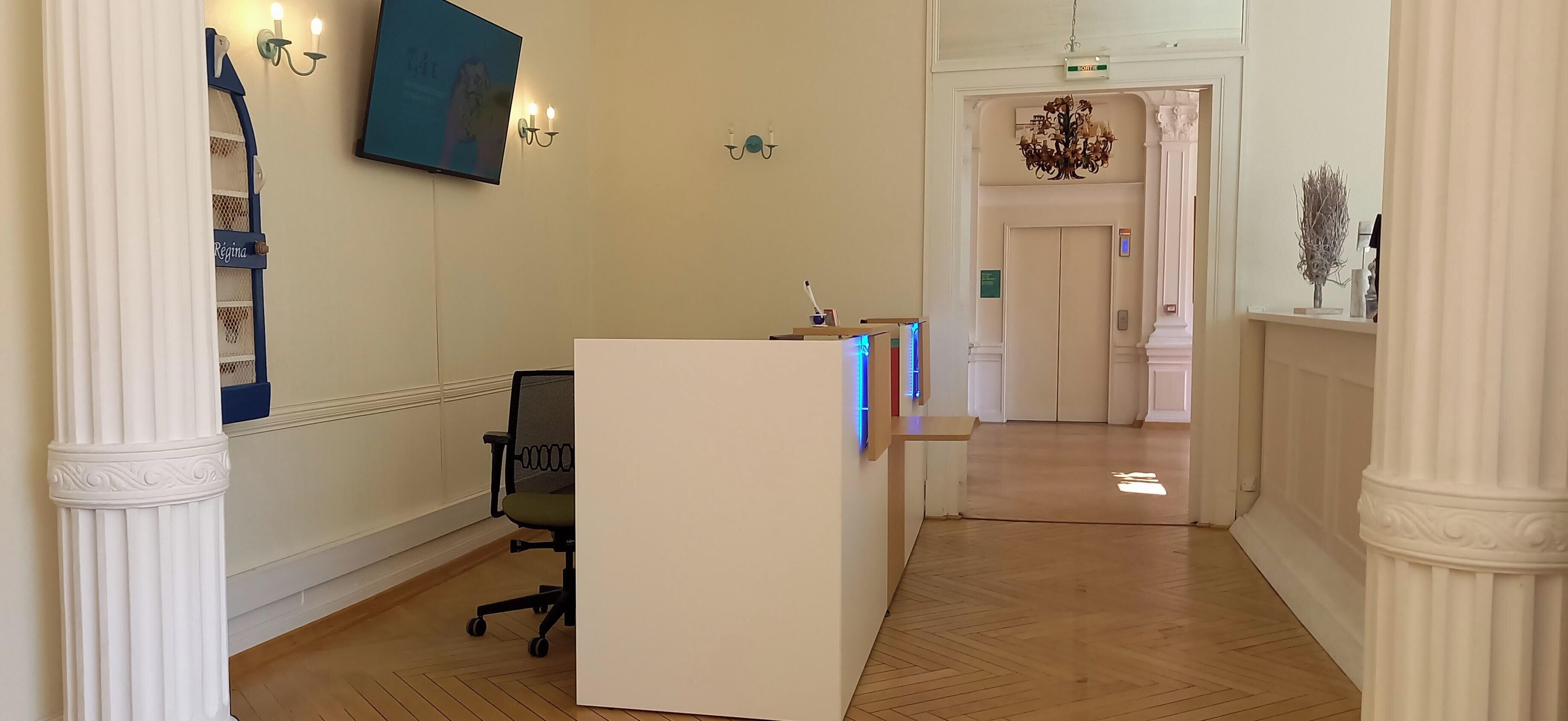 Ein Hotel-Empfangsbereich mit Empfangstresen, einem Sessel, einer Chandelierleuchtre und einem Flur zum Aufzug.