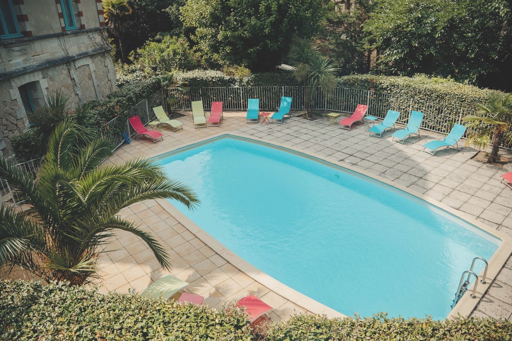 Una piscina rectangular con solárium empinado y azulejos, rodeada por una cerca metálica y varias sillas de descanso.