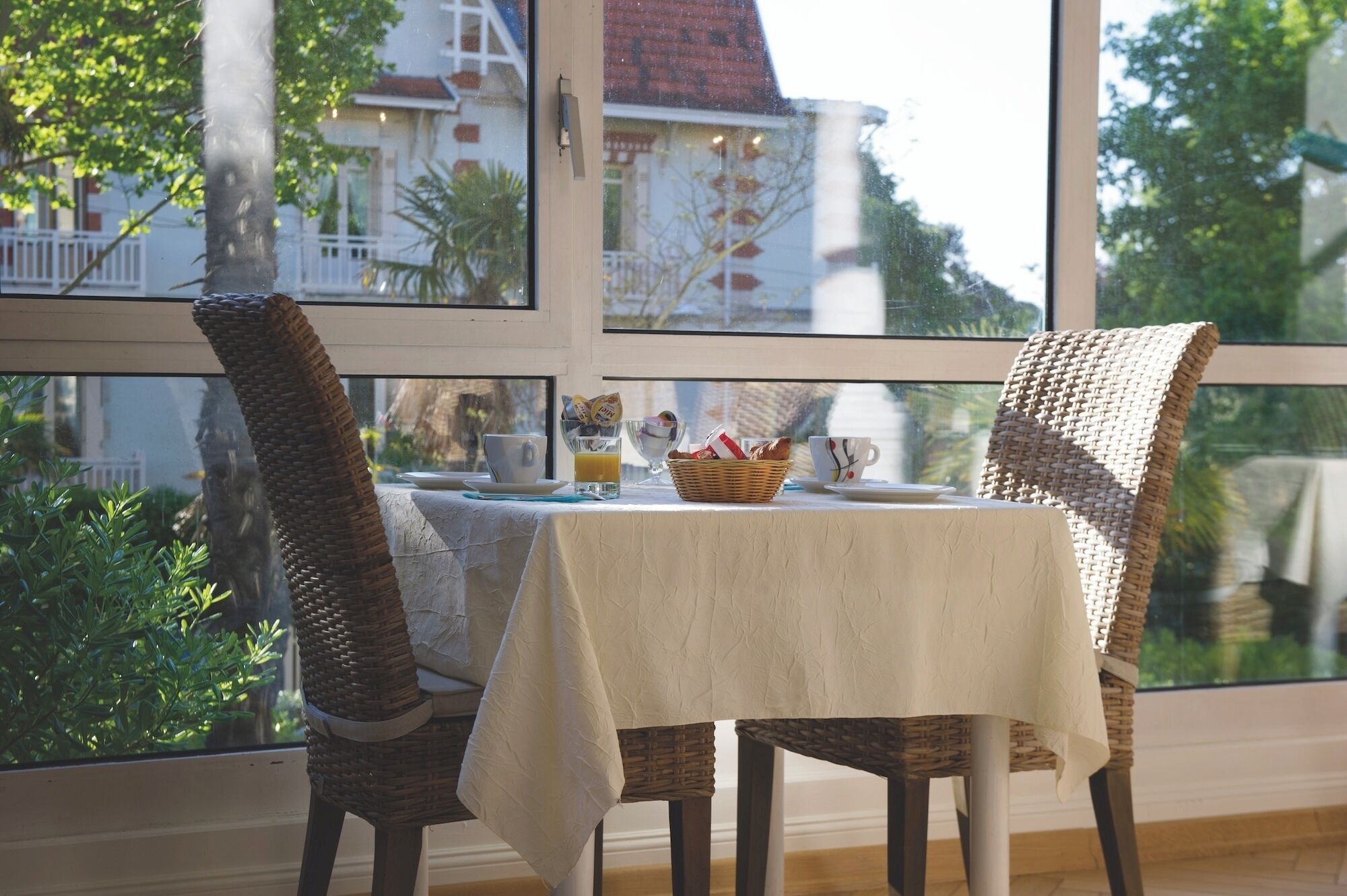 Ein Esstisch mit weißer Tischdecke, Korbstühle und einem Korb voller Lebensmittel.