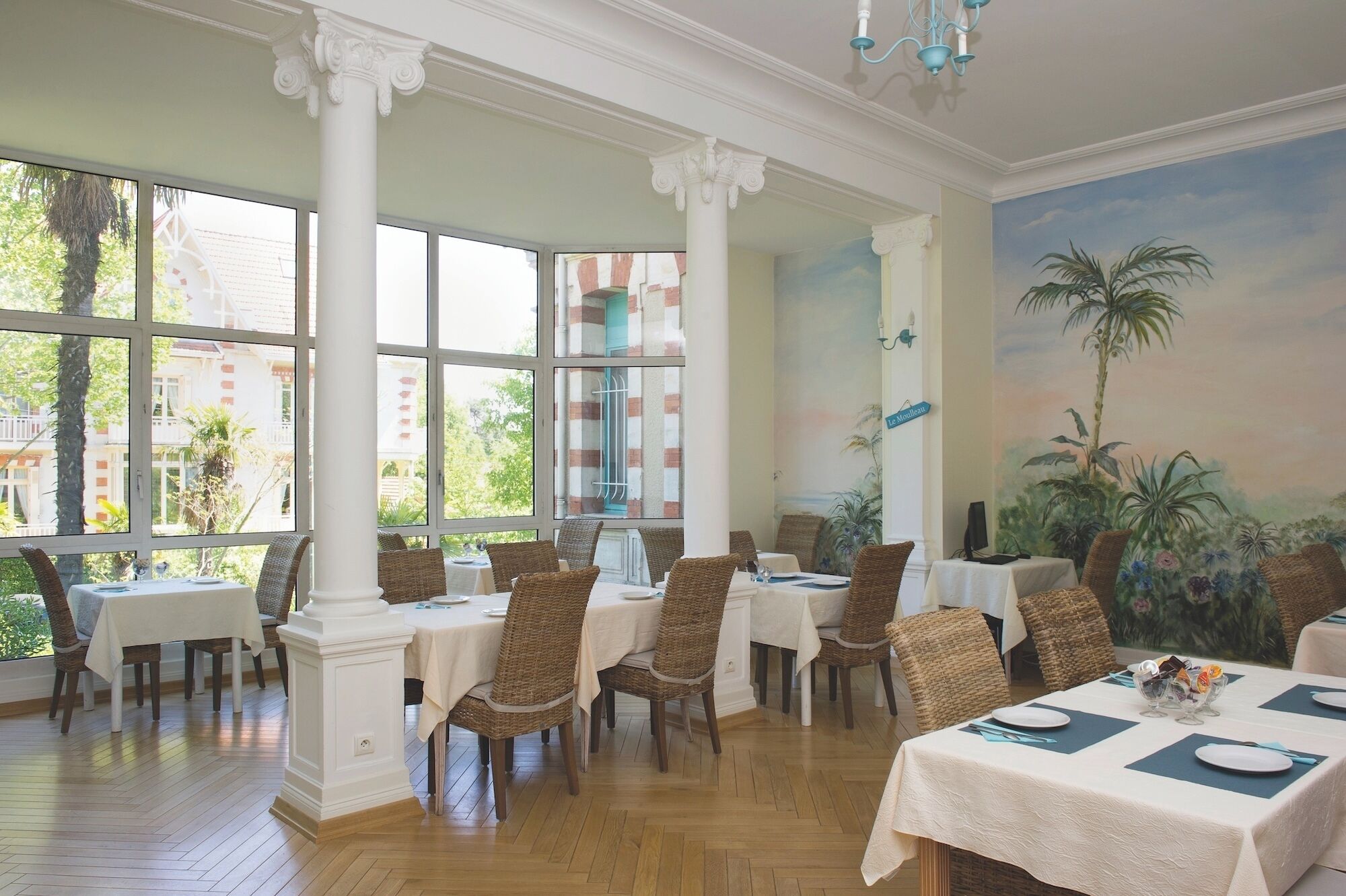 A dining area with tables, wicker chairs, and a mural of a tropical scene.
