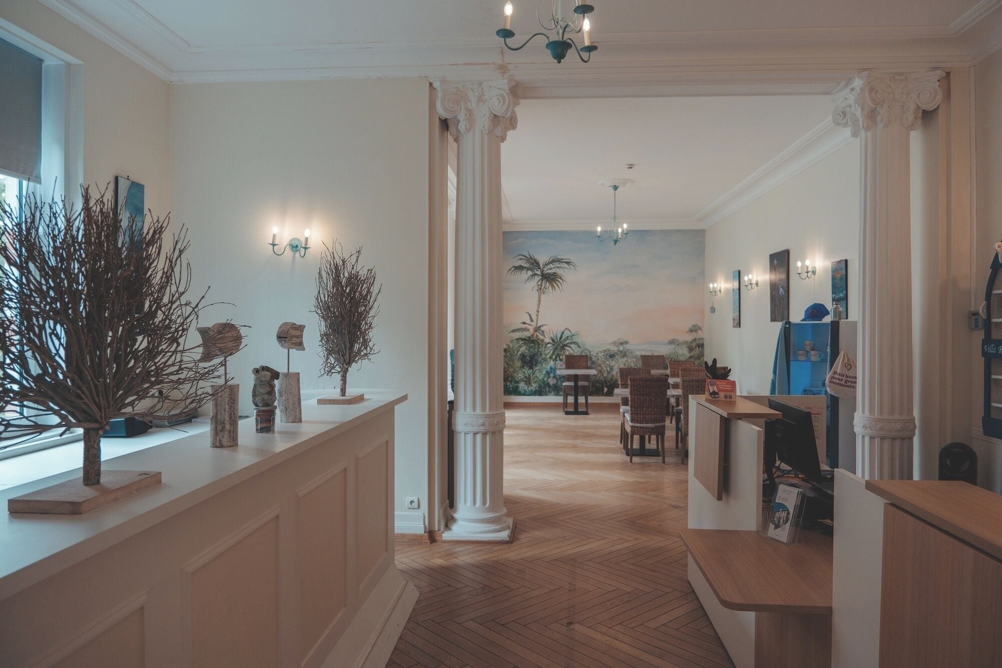 A hotel lobby with a reception desk, seating area, and a mural of a tropical landscape.