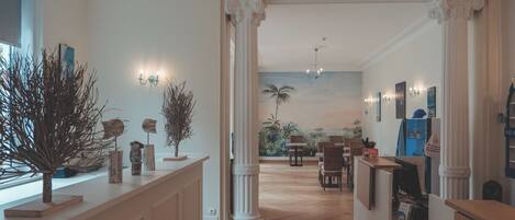 A hotel lobby with a reception desk, seating area, and a mural of a tropical landscape.