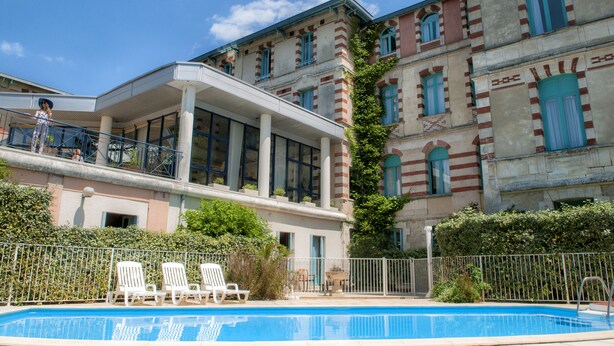 A pool area with lounge chairs, a building with striped facade, and a clear blue sky.