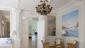A spacious room with a chandelier, a painting of a landscape, and wicker furniture.