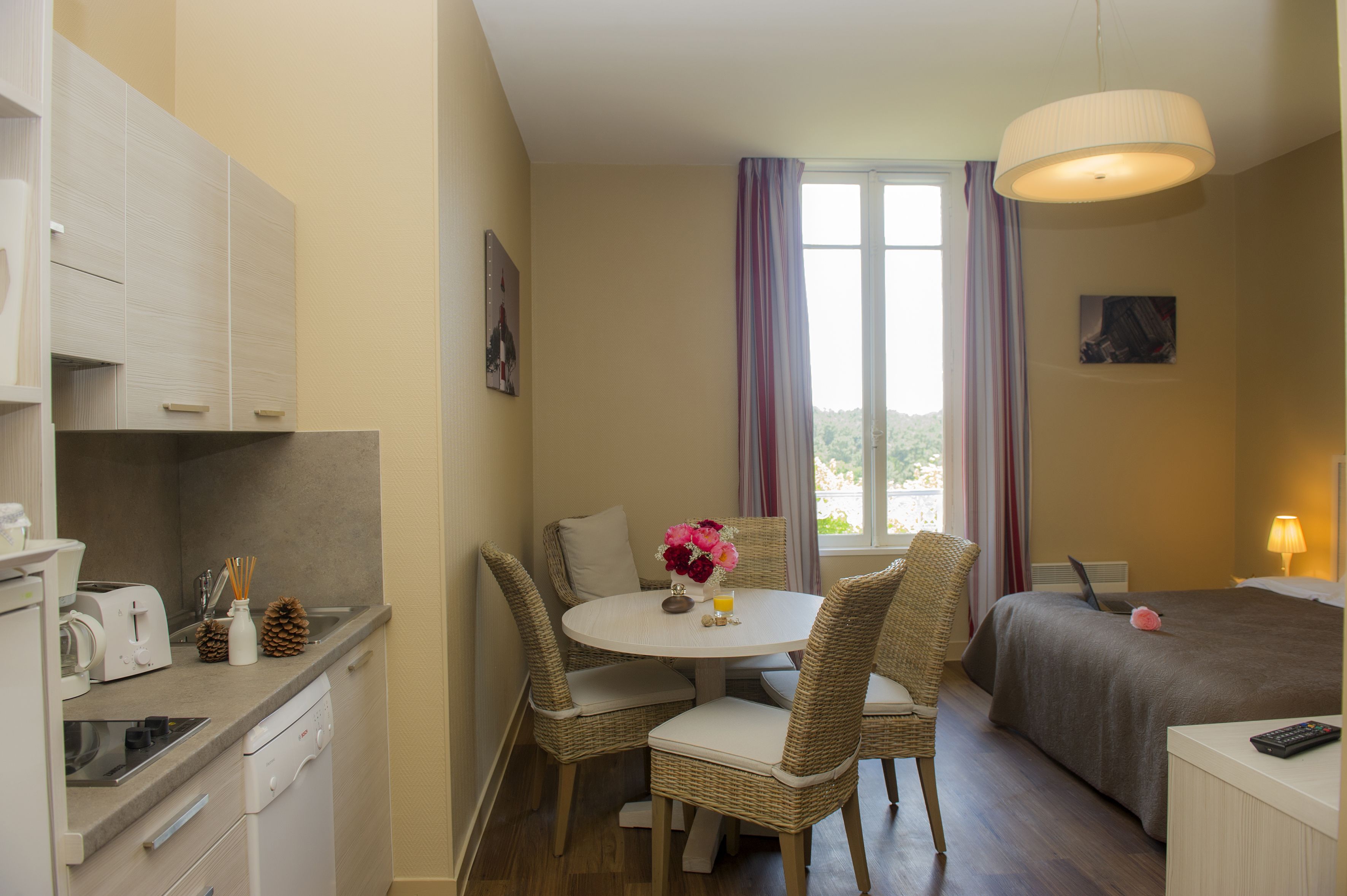 A compact hotel room with a kitchenette, dining area, and a bed.