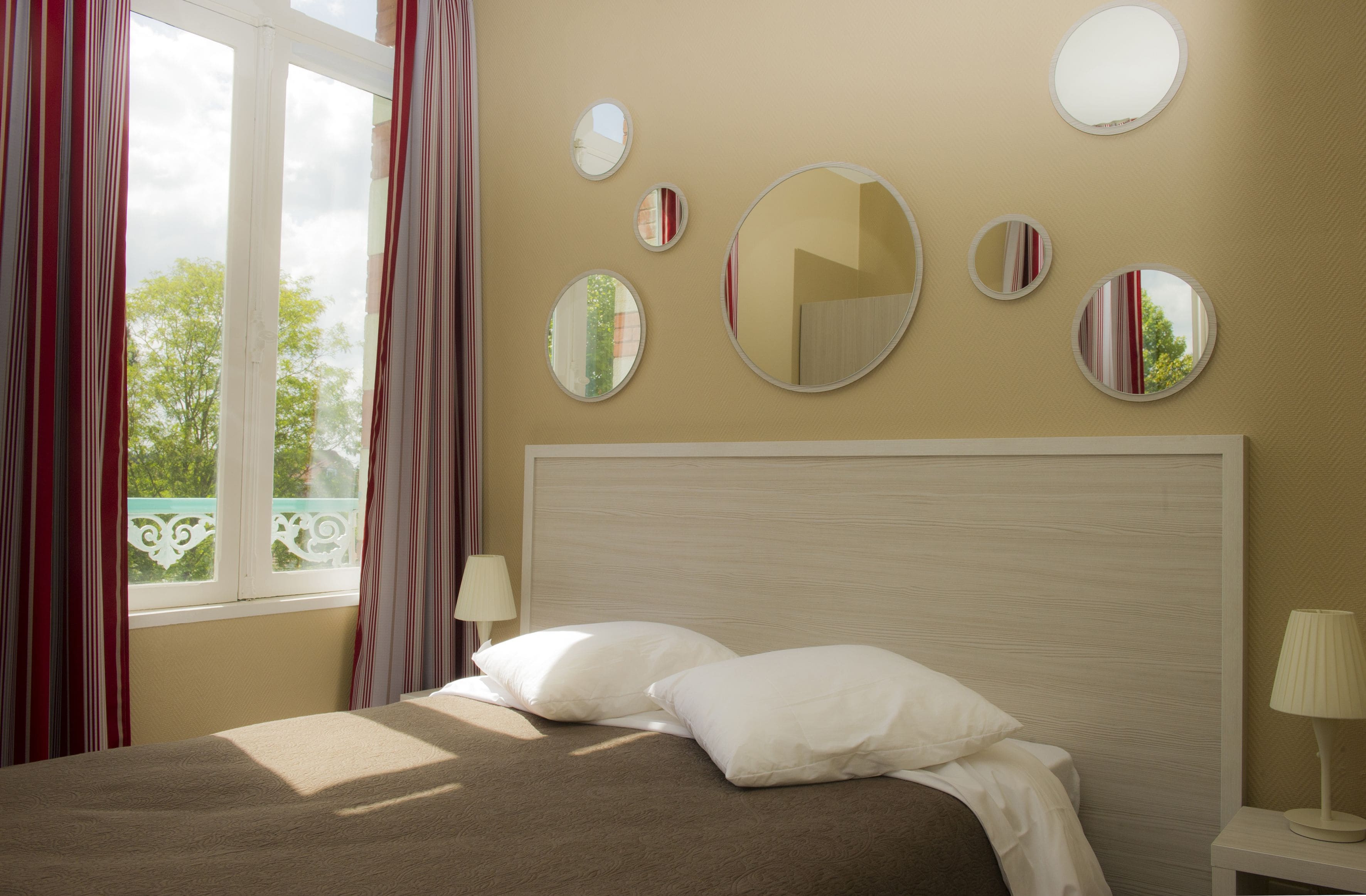 A hotel room with a bed, a nightstand, a lamp, and a window with curtains.