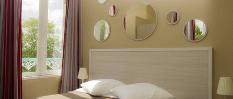 A hotel room with a bed, a nightstand, a lamp, and a window with curtains.
