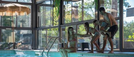 A pool area with clear glass walls, a ladder, and a thatched umbrella.