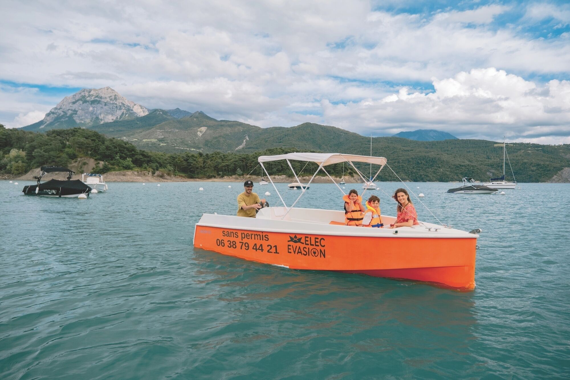 A boat with people on it, a mountainous backdrop, and calm water.