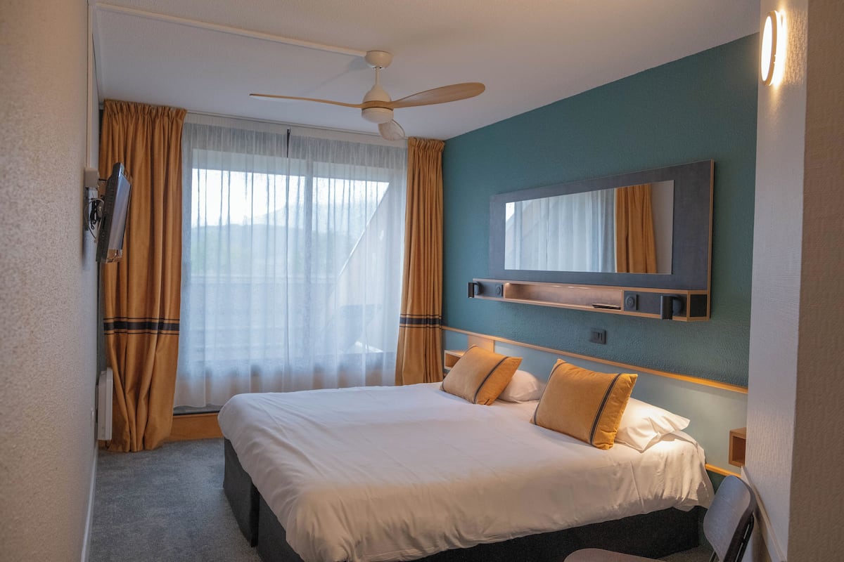 Een hotelkamer met een bed, een plafondventilator, een spiegel en een raam met gordijnen.