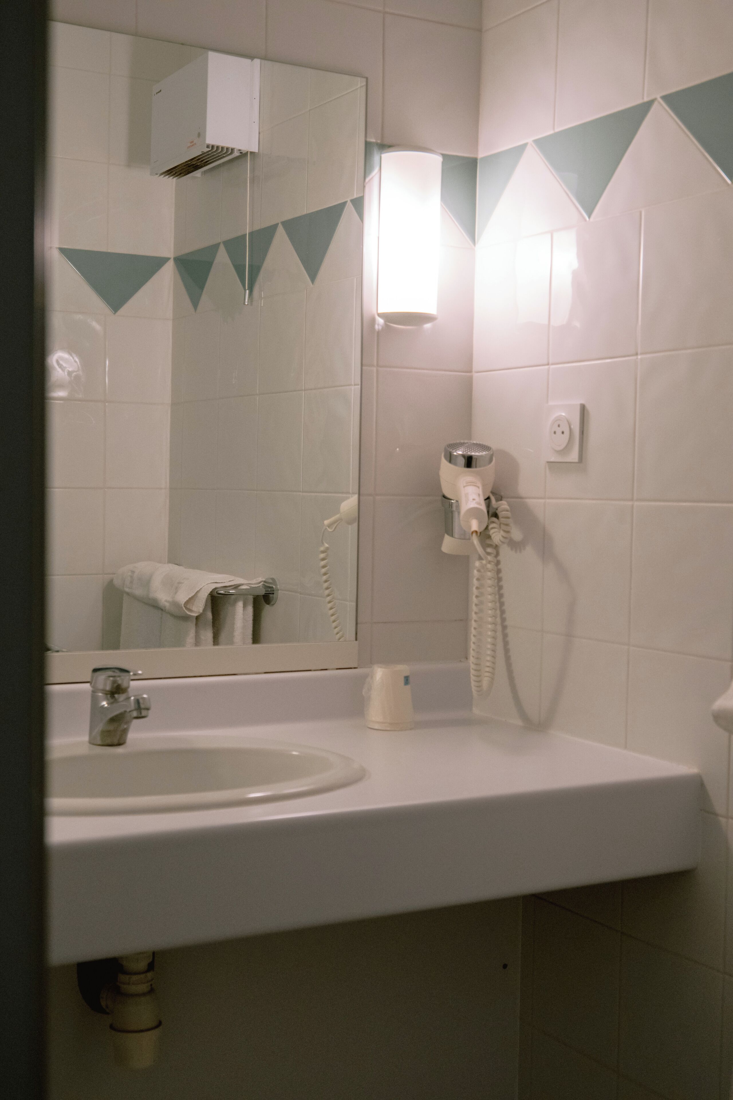 Un baño con lavamanos, espejo y secador de pelo fijado a la pared.
