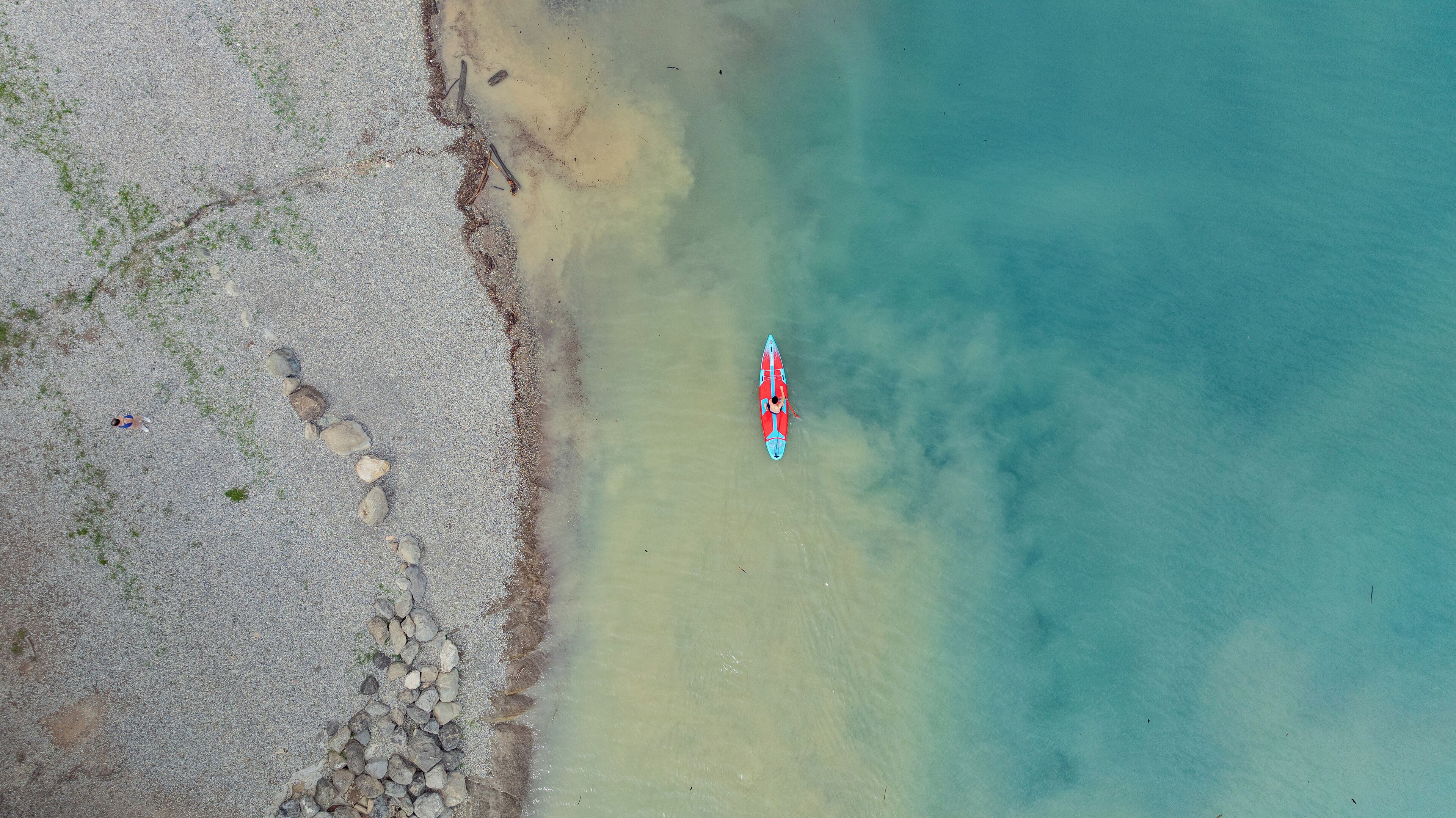 An aerial view of a beach with a surfboard and a person lying on the sand.