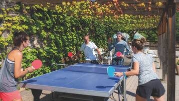 A ping pong table set up outdoors with a wooden pergola and green foliage in the background.