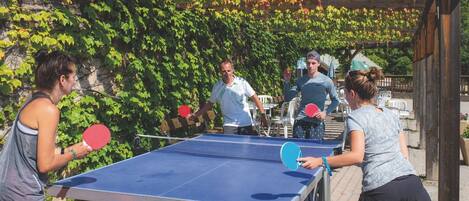 A ping pong table set up outdoors with a wooden pergola and green foliage in the background.
