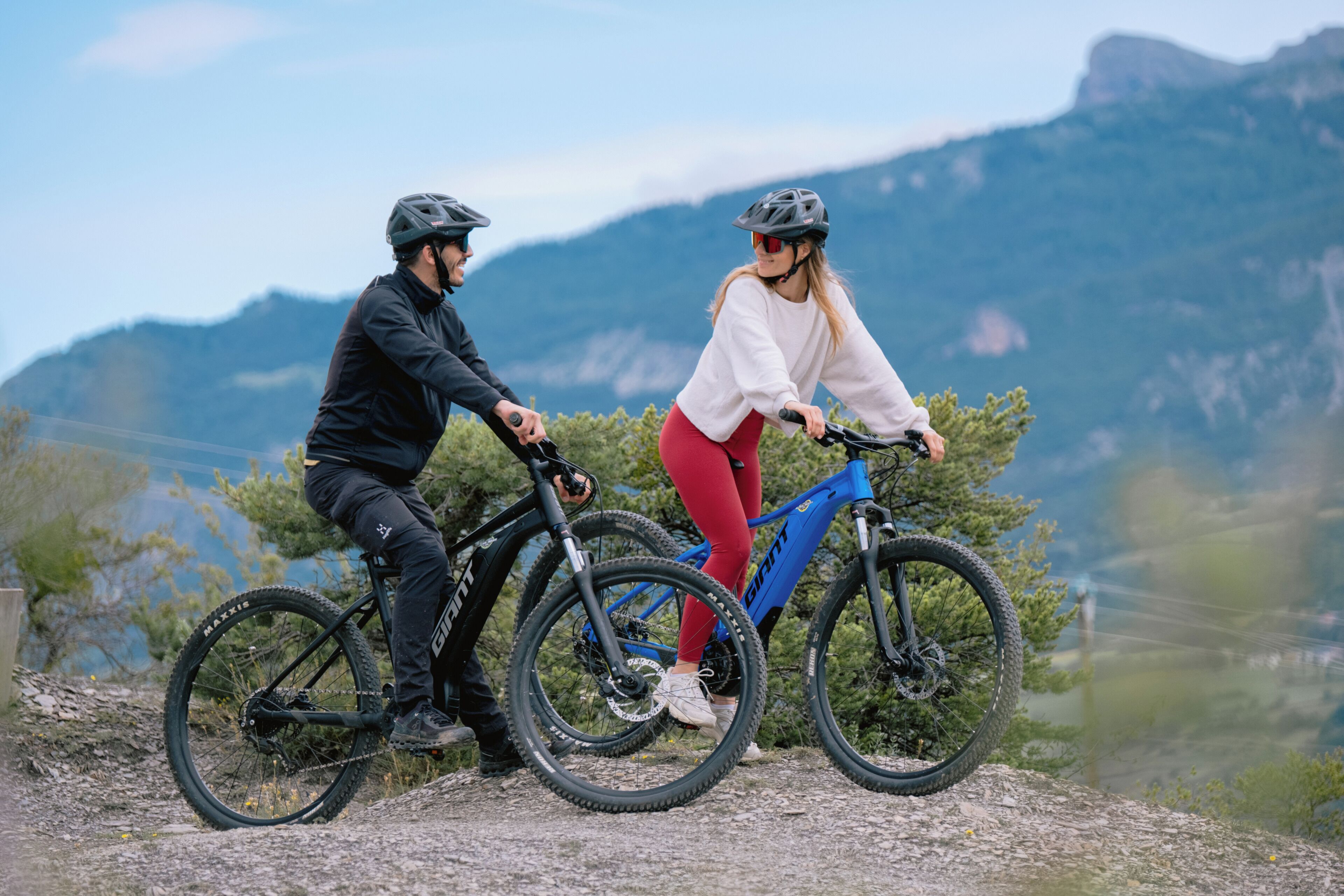 Two people on bicycles on a mountain trail with a clear view of the surrounding landscape.