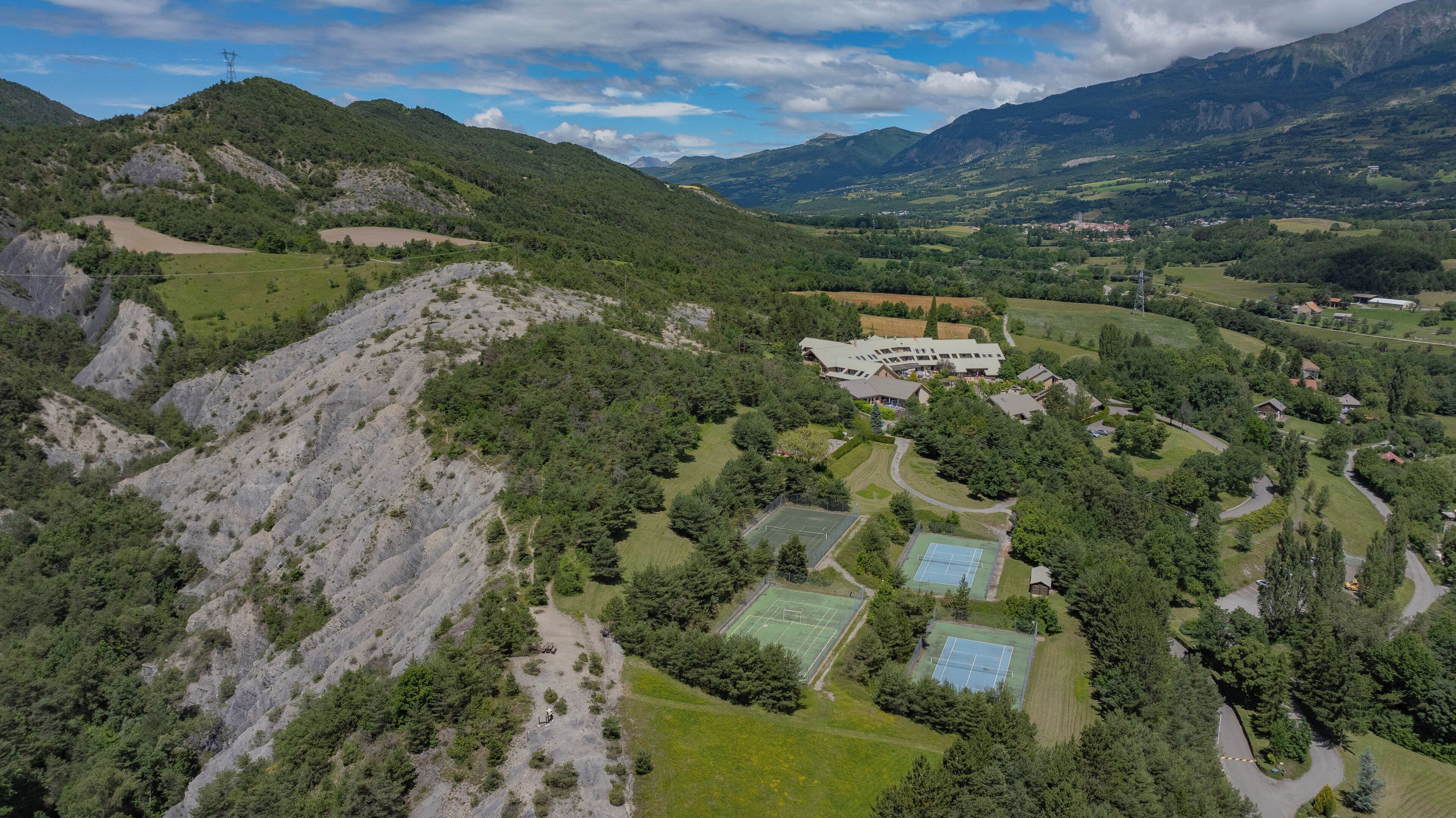 Un paysage montagneux avec une zone résidentielle comprenant des maisons, des courts de tennis et un grand bâtiment doté de nombreuses fenêtres.