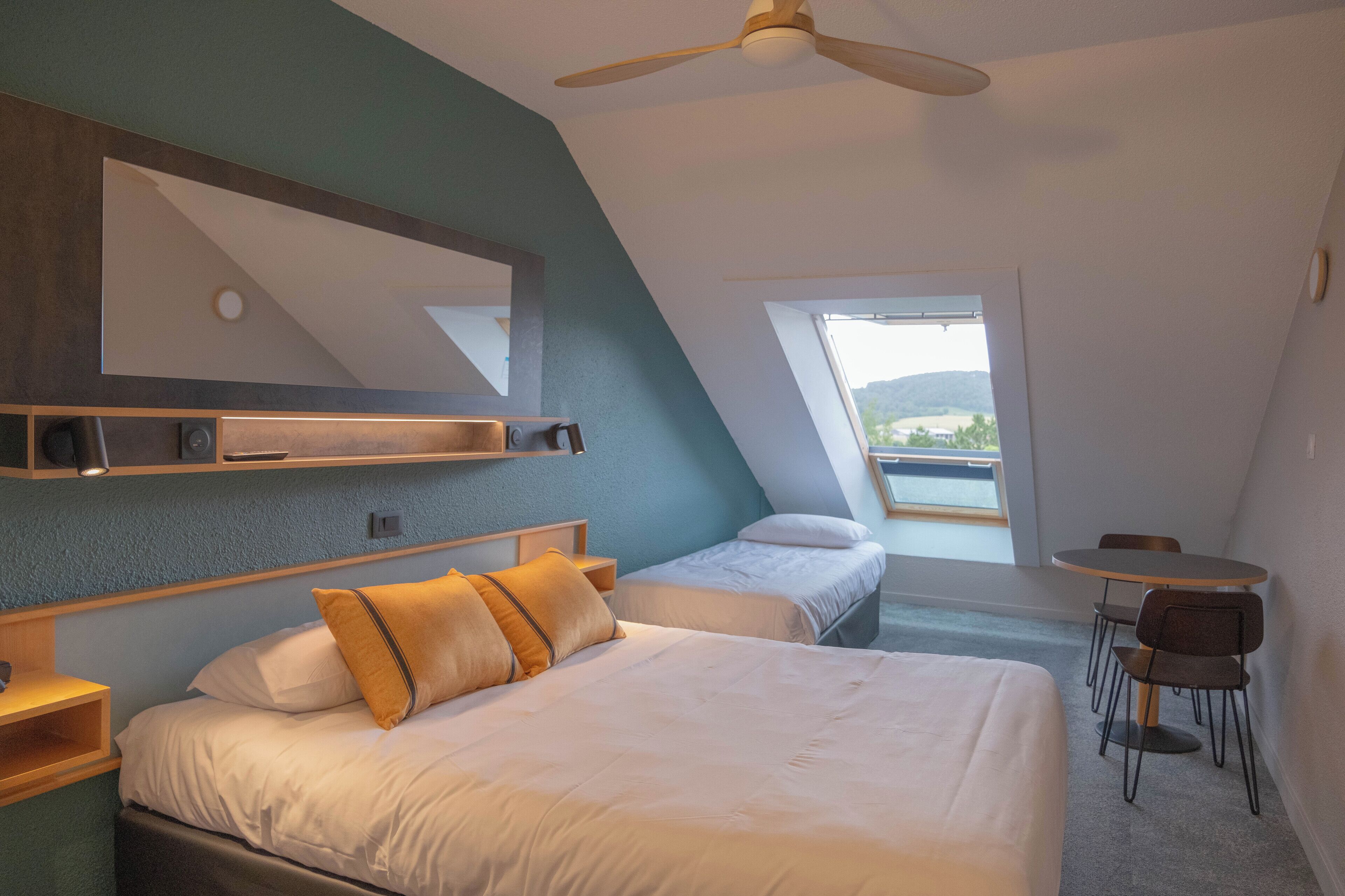 Un dormitorio con una cama grande, una cama más pequeña, un escritorio y una silla. Hay una ventana con vistas al exterior.